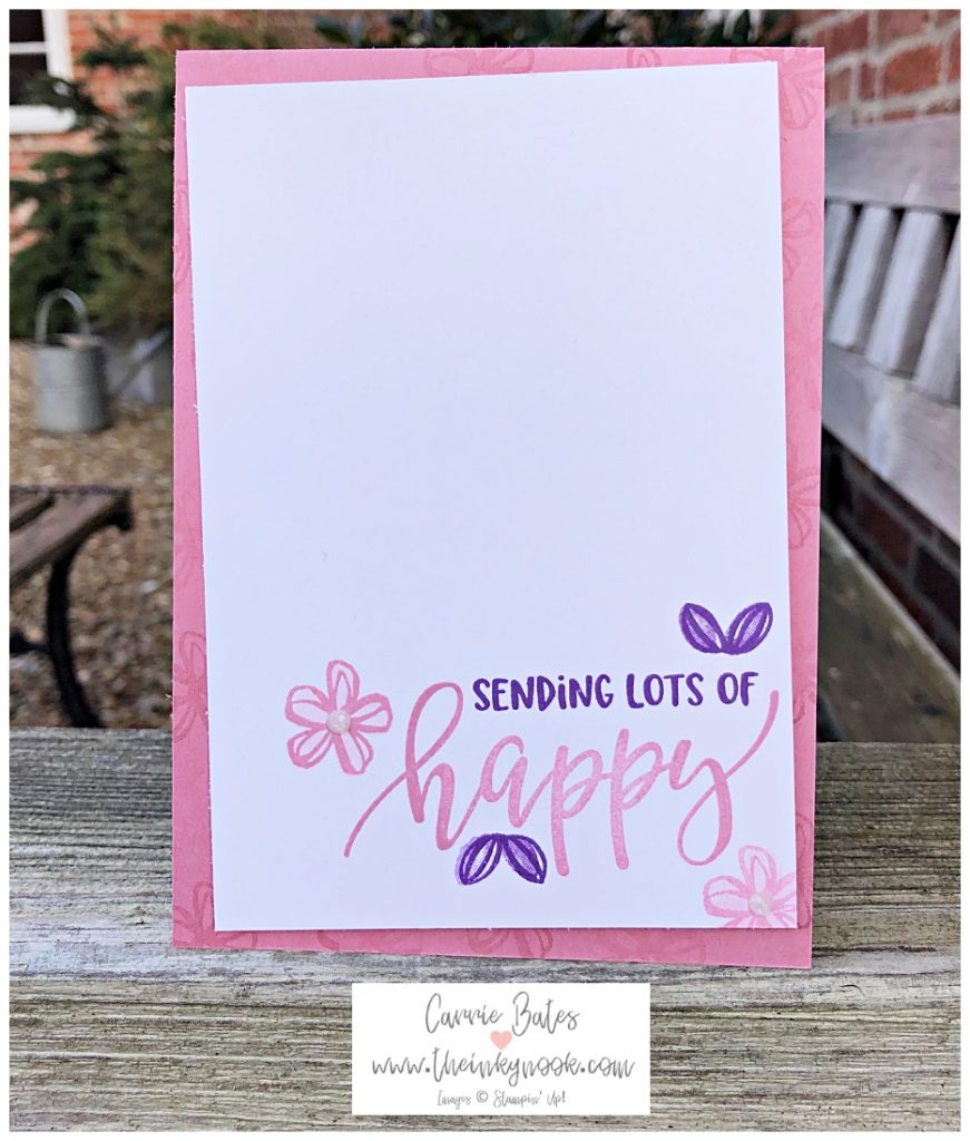 Pink card base stamped with daisy style flowers and topped with a whisper white layer.  The white layer has the words Sending lots of happy.  Sending lots of is stamped in purple ink and is capital letters.  The 'happy' is stamped underneath n pink and is a swirly hand written font.  The words are in the bottom right hand corner of the white layer.  They are framed by two pink flowers topped with a white sparkling gem and two purple leaf duos at the top and bottom.  This is a happy card to send to a friend.