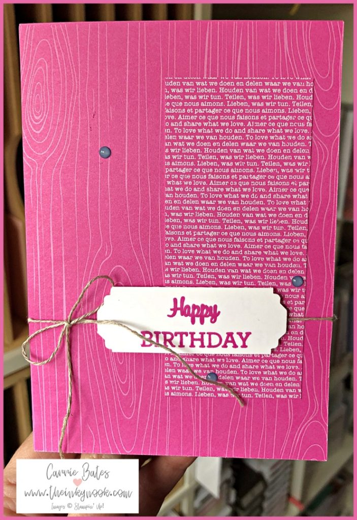 Simple birthday card which is Merry Magenta Madness in colour.  The card has a woodgrain effect designer series paper layer which fills the card base.  This is topped with a narrow rectangle also made from designer series paper.  This paper is filled with font in european languages which in English reads "To love what we do".  A twine string bow is tied with long tails and then topped with a Happy Birthday sentiment towards the bottom right hand corner.  Then 3 Misty Moonlight enamel dots are randomly placed on the card.