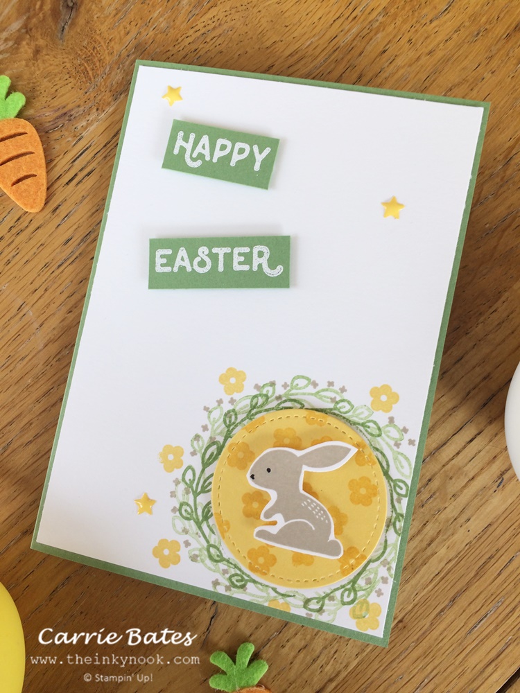 Handmade green Easter card topped with a white layer.  In the top left hand corner of the card there is "Happy Easter" stamped and embossed in white .  Brown bunny stamped and cut out and glued on to yellow stitched framed circle stamped with flowers. This is framed by a leaf wreath stamped around the edge and randomly stamped yellow flowers. Easter craft inspiration