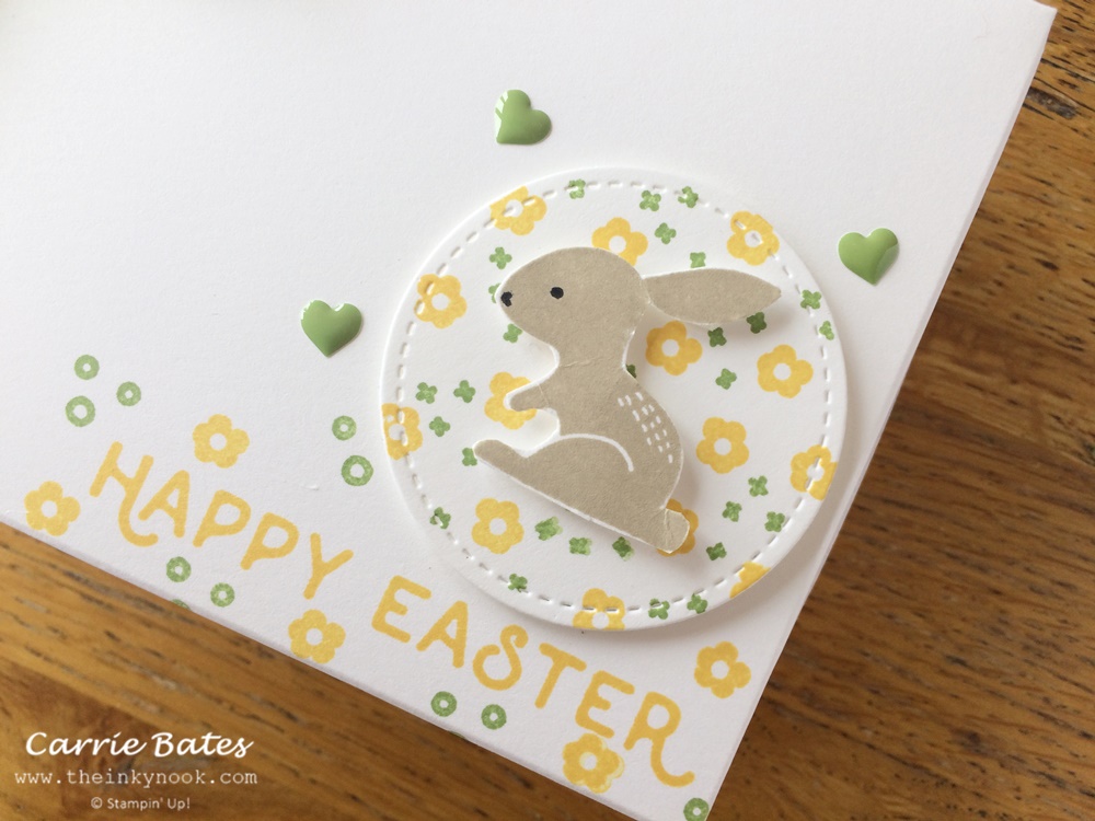 Close up of handstamped Easter bunny topped on a stitched circle stamped with mini yellow flowers and mini green clover leaves.  'Happy Easter' stamped in yellow just below this circle and 3 green enamel hearts placed around.