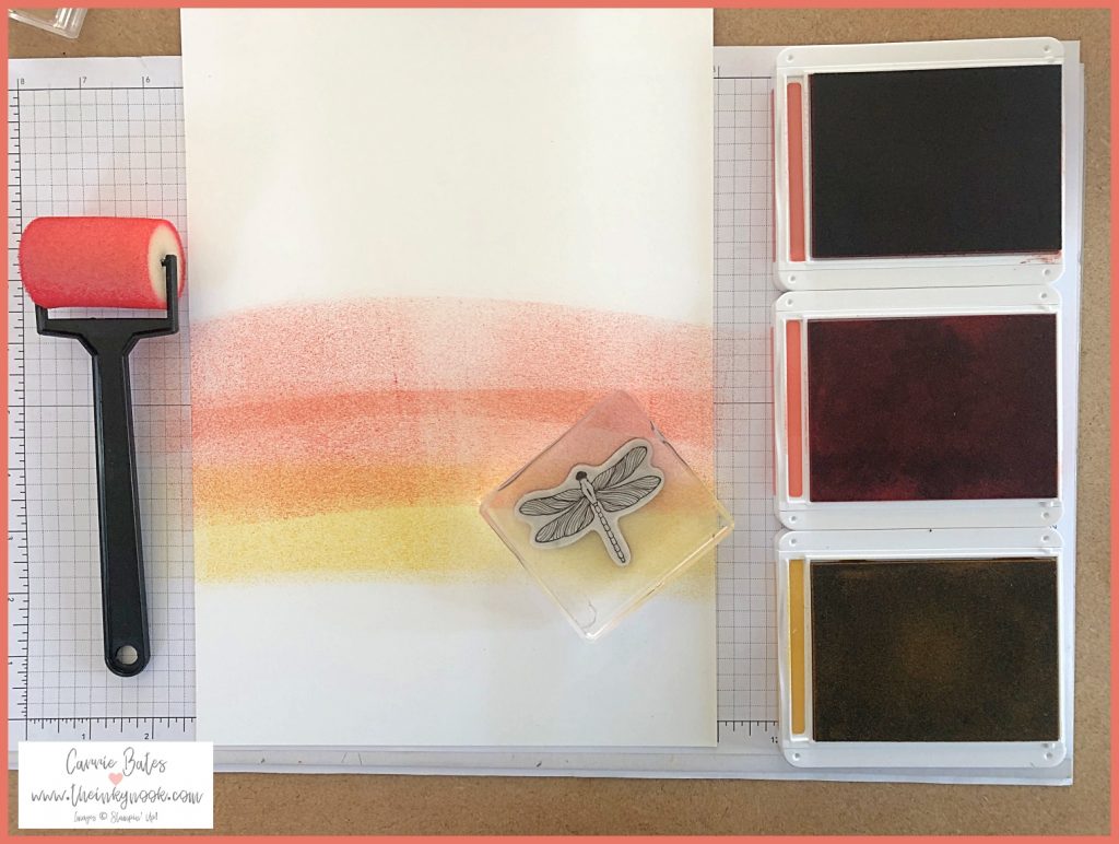 Sheet of white cardstock partially covered with tones of orange and yellow to create a rainbow effect with 3 ink pads along the right hand side and a sponge brayer on the left.  Image shows how to use sponge brayering for cardmaking