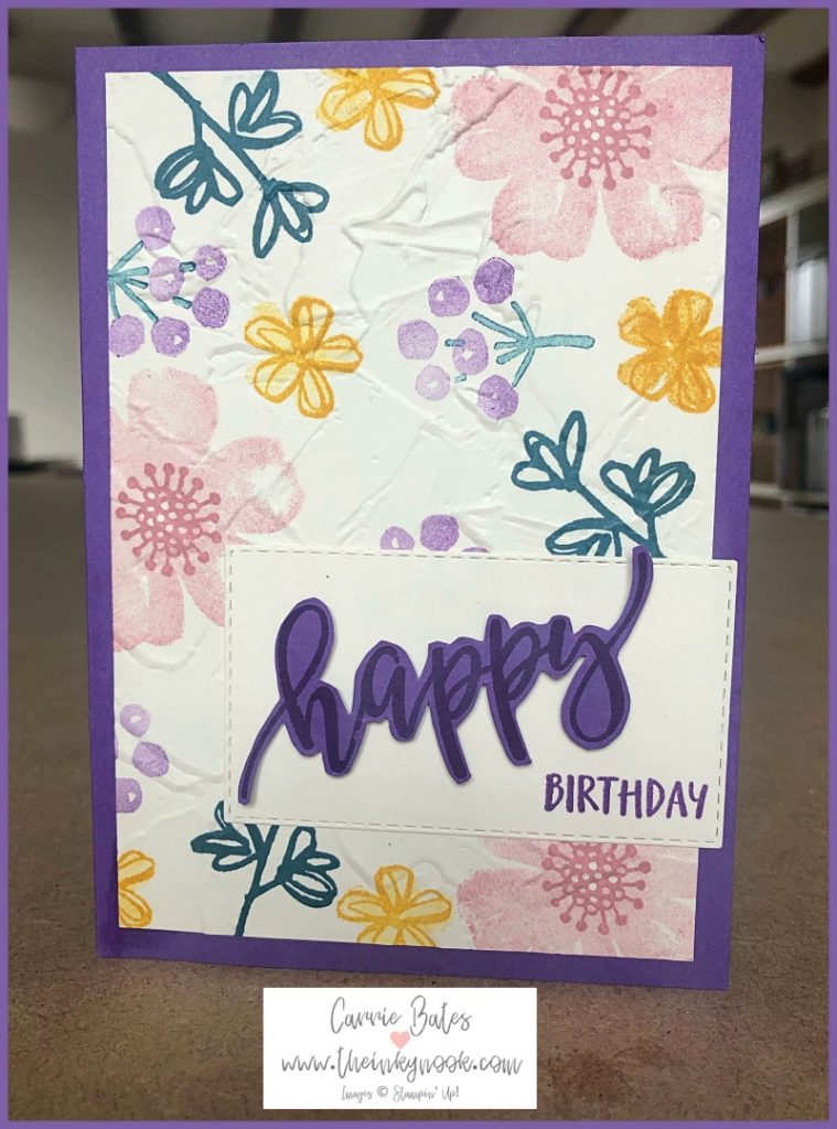 Handmade floral birthday card with a purple card base.  A vanilla painted texture layer is stamped with pink and yellow flowers and some purple seed heads with green leaves.  This is topped with a swirly purple 'happy' word and a stamped upper case 'birthday' word