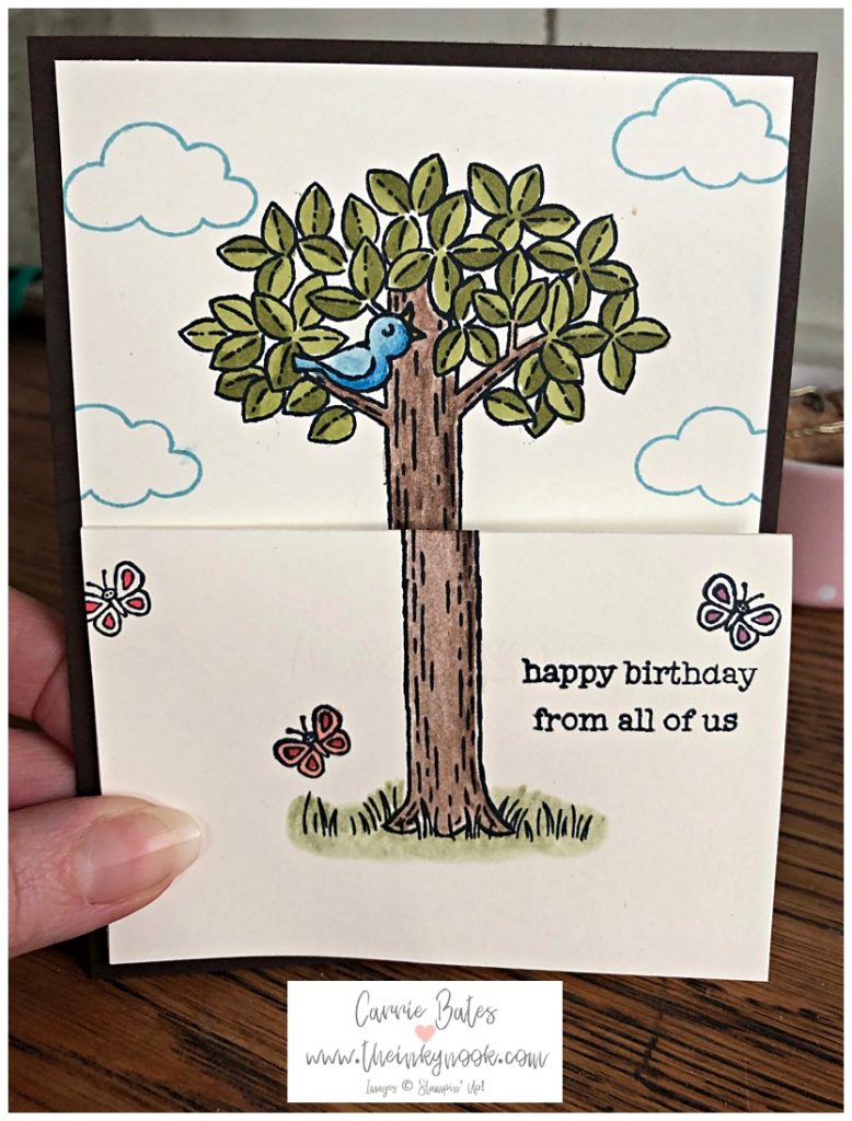 Front closed view of  children's fun fold card.  This view shows a small tree with green leaves and a brown trunk with a bird singing on a branch.  There are blue clouds and some butterflies fluttering.  The sentiment reads ' happy birthday from all of us'