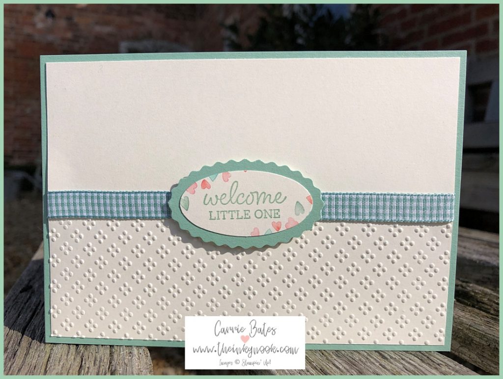 Green welcome baby card with vanilla layer.  The bottom half of the card is embossed with little dots. There is a strip of green gingham ribbon across the front topped with a 'welcome little one' label bordered with mini coloured hearts.