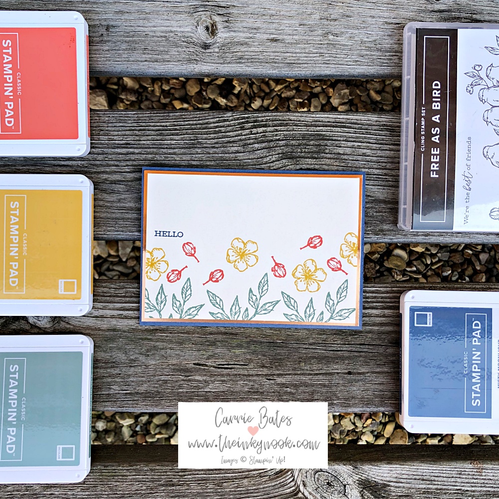 Flatlay showcasing a card made with Autumn colours. Image shows a blue card base and stamped flowers, buds and leaves in yellow, coral and green. The card is surrounded by 4 ink pads in the card colours and the stamp set