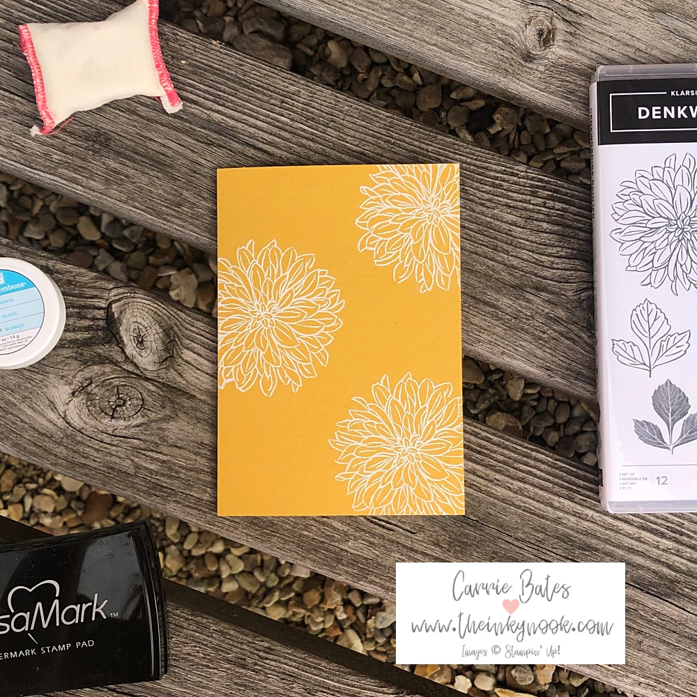 Flatlay picture showcasing a yellow card  stamped with white dahlia flowers using heat embossing.