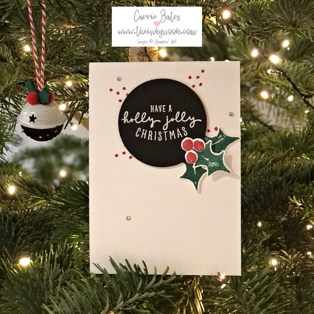 White card base topped with black circle with white writing saying "have a holly christmas" Then three green holly leaves topped with red berries in the bottom right corner of the circle.