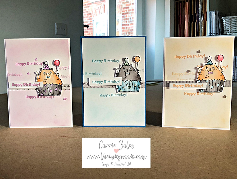 Row of three cards showing a cat sat in a spotty cupcake case holding a balloon. Two of the cards have orange cats with grey cupcake cases and the middle card has a grey cat sat in a blue cupcake case. Three cute cat birthday cards.