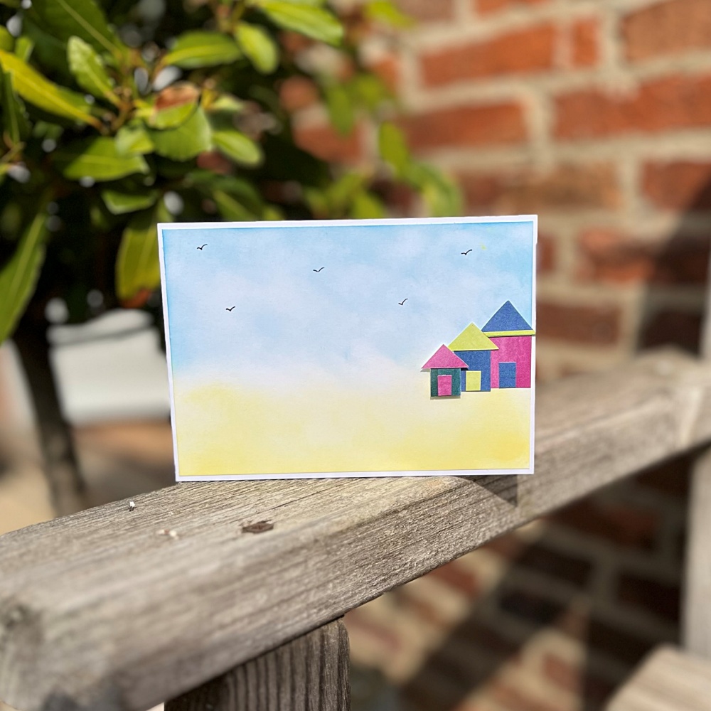 Cute beach hut card with watercolour effect background to create a beach and skyline.