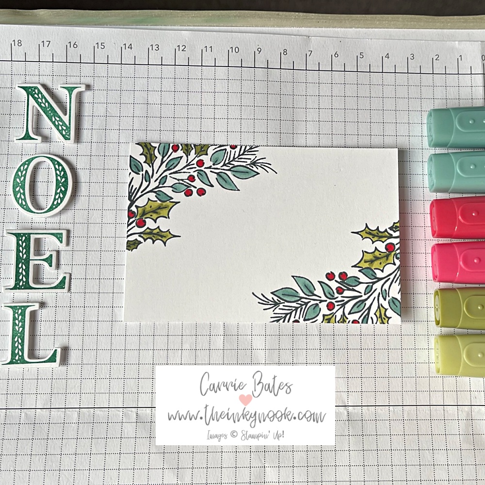 Stamped image of holly leaves and berries with red, green and blue-green pens and the word NOEL cut out.