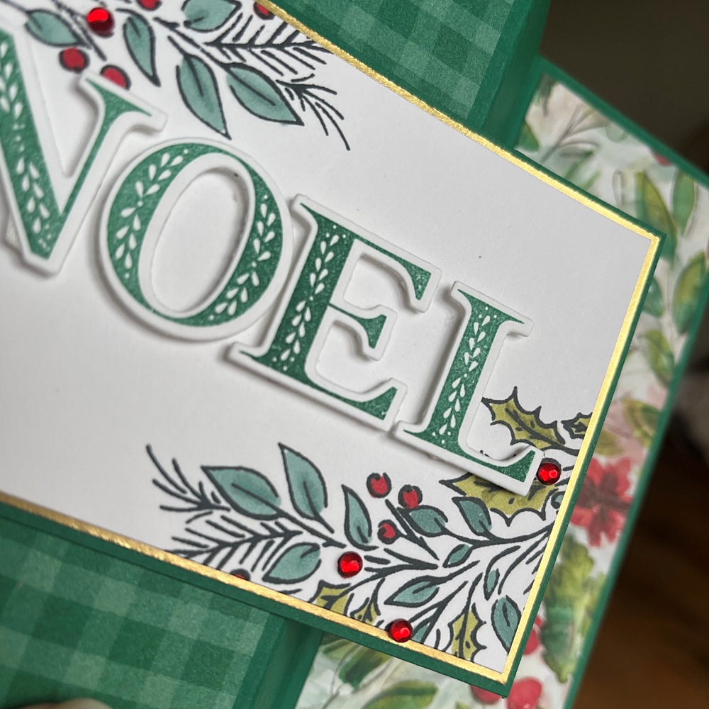 Close up of the word "NOEL" in green letter on top of a white layer with coloured holly and berries with some little red sparkle rhinestones on the berries