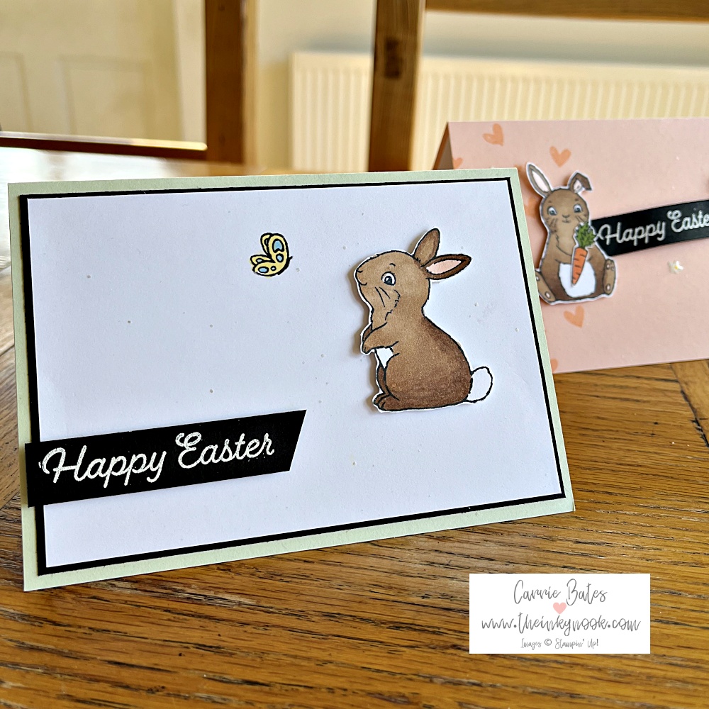Simple Easter card created on a soft green card base with a brown bunny sat looking at a yellow and blue butterfly. A greeting in white on a black card banner reads "Happy Easter"